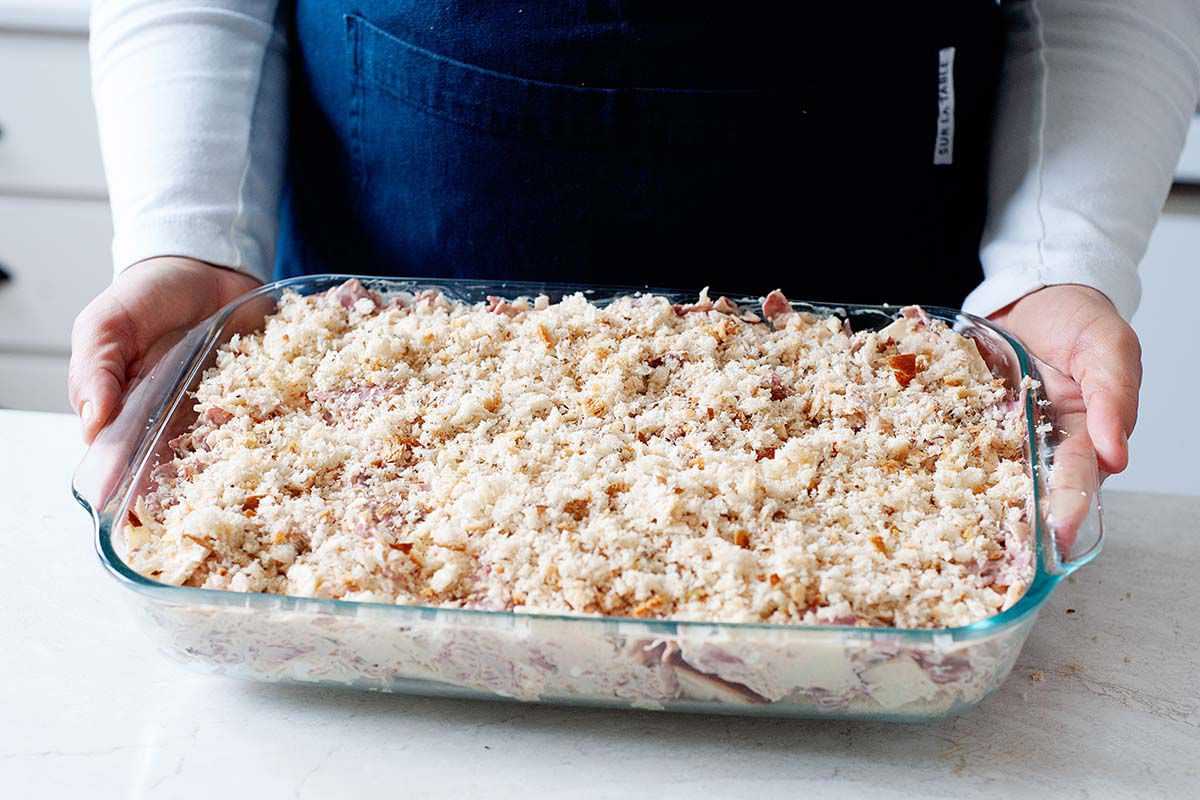A person is holding a glass casserole dish with pastrami reuben unbaked inside.