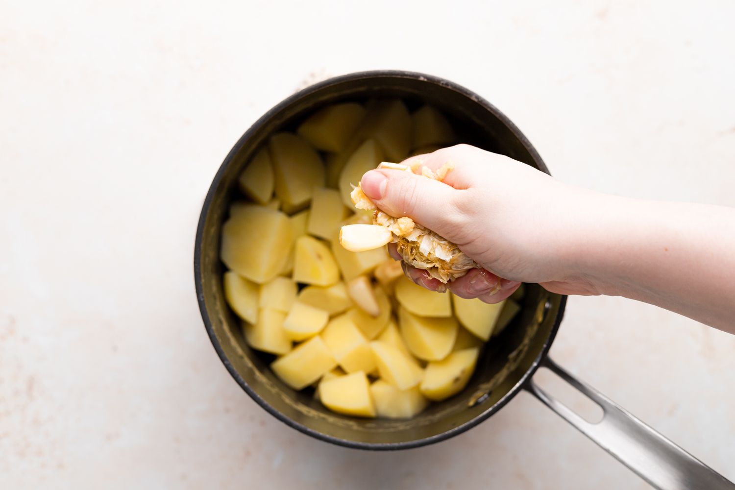 Adding roasted garlic to a pot of potatoes to make roasted garlic mashed potatoes.