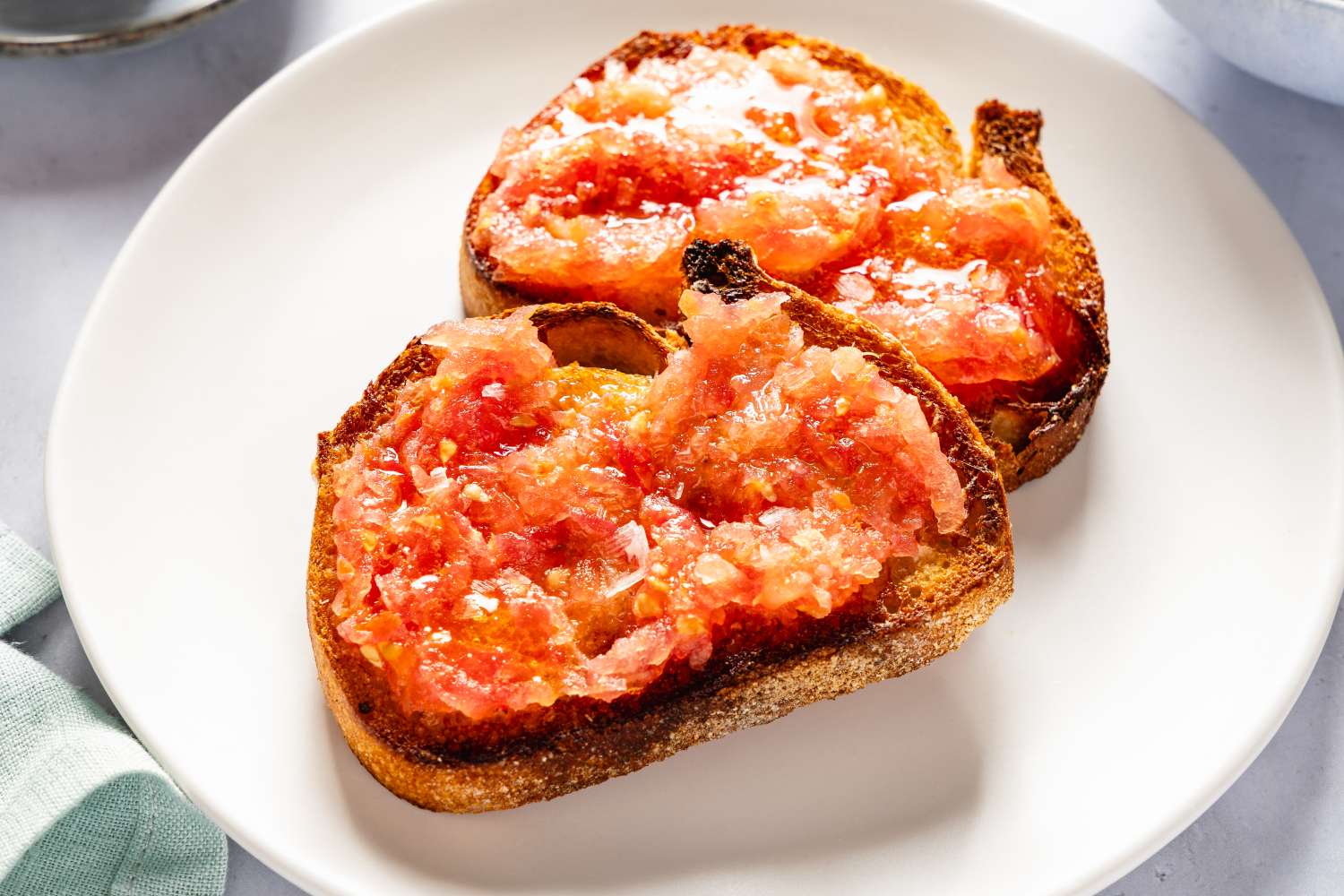 Two slices of toasted bread topped with crushed tomato served on a white plate