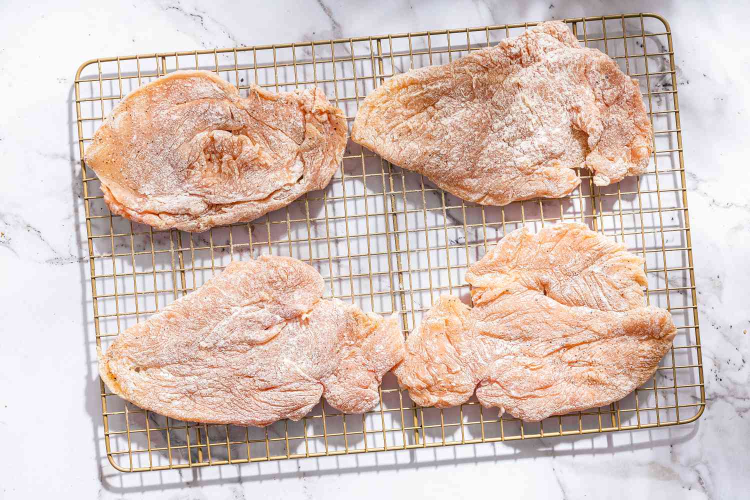 flattened out chicken cutlets sprinkled with flour resting on a cooling rack for Chicken Romano
