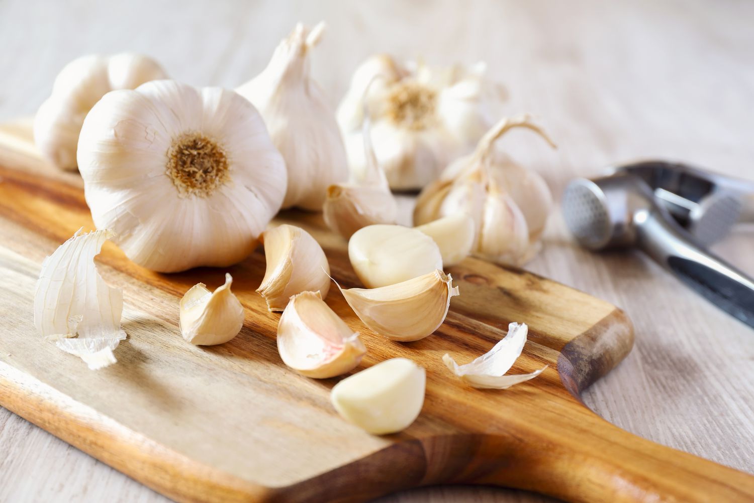 Bulbs of garlic and loose garlic cloves on a cutting board with a garlic press in the background