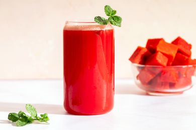 A glass of watermelon batido with mint next to a glass bowl of watermelon cubes