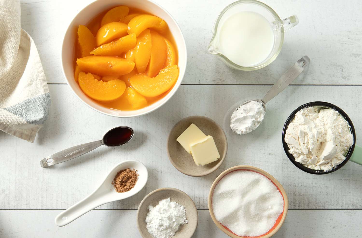 Ingredients for making peach cobbler including sliced peaches milk flour sugar butter vanilla and spices