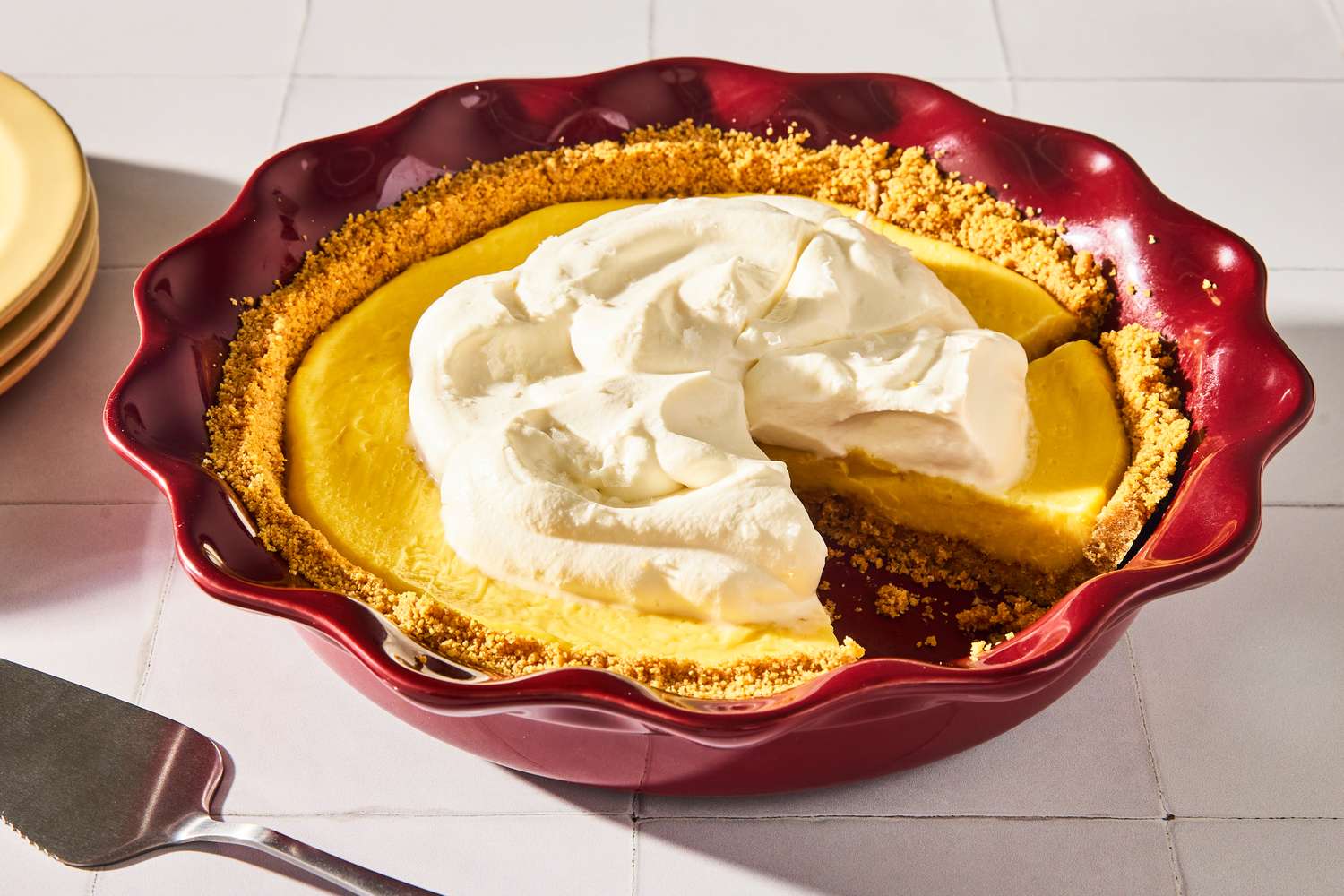 Pie with a whipped cream topping in a red dish and a slice missing
