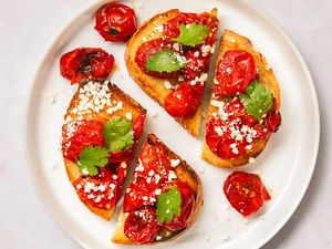 Blistered tomato toast slices garnished with herbs and cheese on a white plate