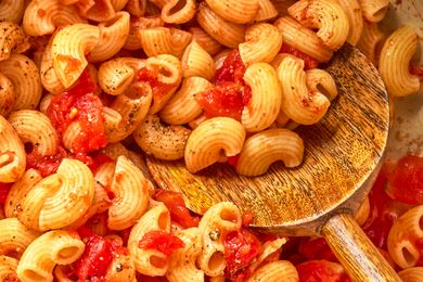 Cooked macaroni with diced tomatoes resting on a wooden spoon
