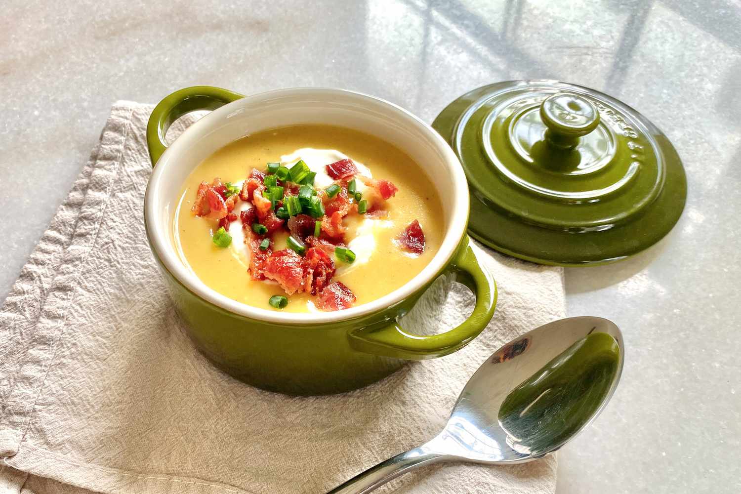 A very creamy-looking potato soup in a small ceramic cocotte. The soup is generously topped with sour cream, green onion, and bacon.