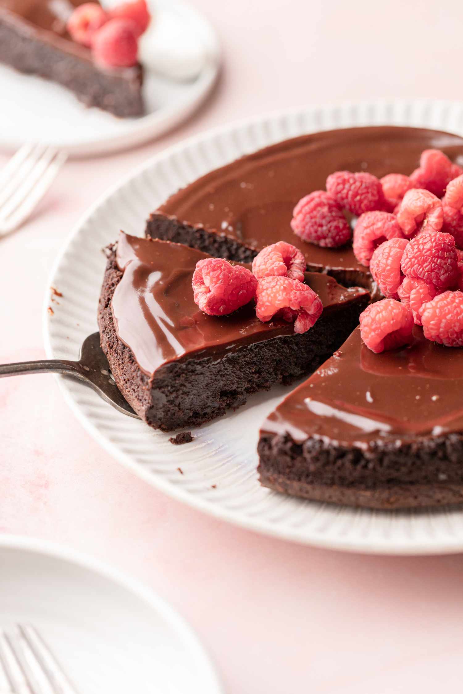 A Slice of Flourless Chocolate Cake Garnished with Fresh Raspberries Lifted on a Pie Server