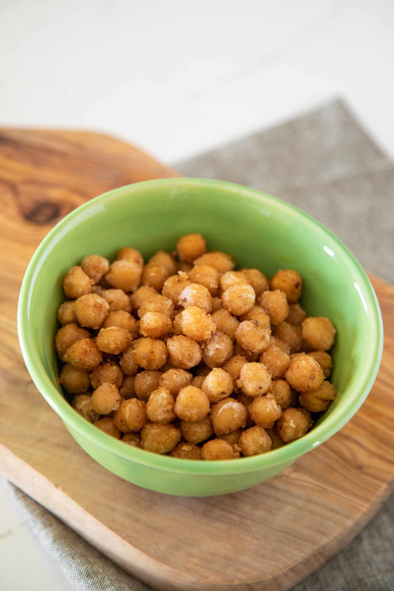 Crispy chickpeas in a green bowl on a wooden platter
