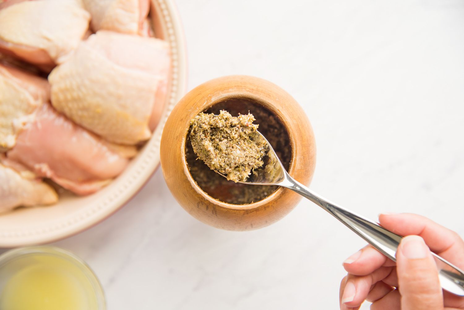 Garlic Paste in a Spoon Removed from a Mortar and Pestle Next to a Plate of Chicken Pieces for Pollo Guisado Recipe