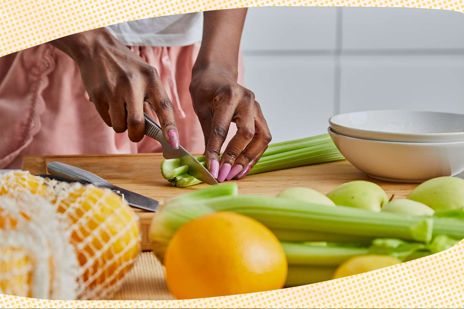 A person cutting celery on a cutting board next to a stack of bowls. In the surroundings, more produce (more sticks of celery, apples, oranges, and a bag with more oranges). Around the photo, fund yellow and white dotted illustrations