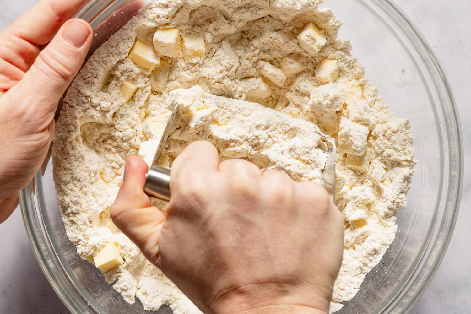 Hands using a pastry cutter to mix dry ingredients with the butter in a bowl for Chocolate Chip Scones recipe