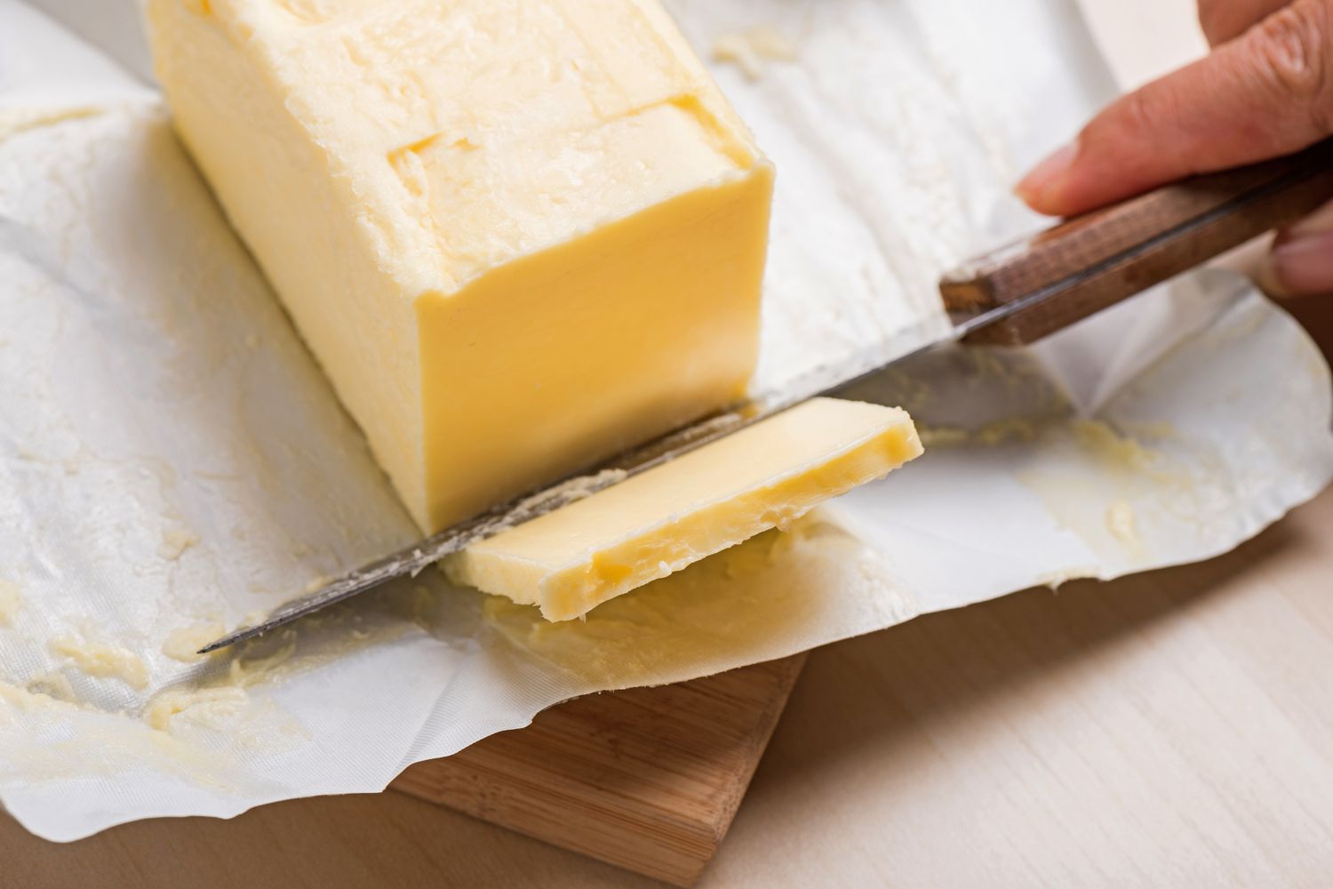 A hand slicing a stick of butter on parchment paper with a knife