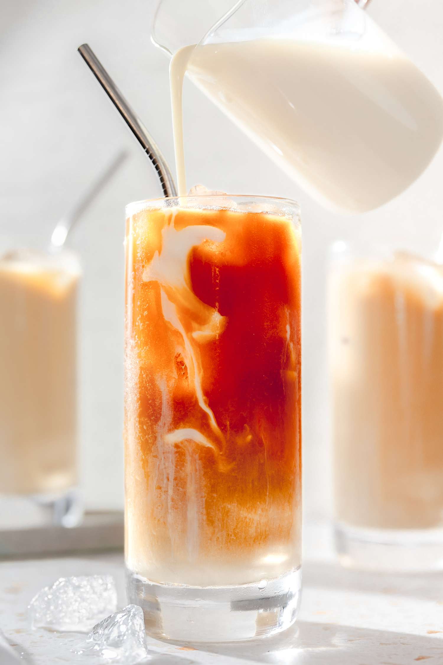Milk Poured Into a Glass of Thai Tea from a Creamer, and in the Background, More Glasses of Thai Ice Tea