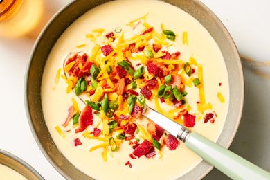 Bowl of loaded potato soup garnished with shredded cheese scallions and bacon with a spoon