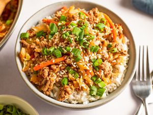 Angled view of a bowl of egg roll in a bowl next to two forks and bowl of sliced green onions