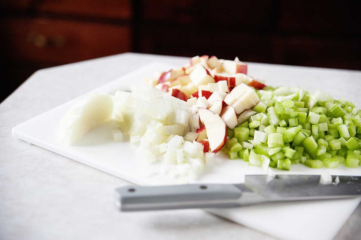 Apples, onions, and celery on diced on a cutting board for easy thanksgiving stuffing.