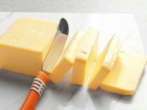 A block of butter being sliced with a knife resting on a marble surface