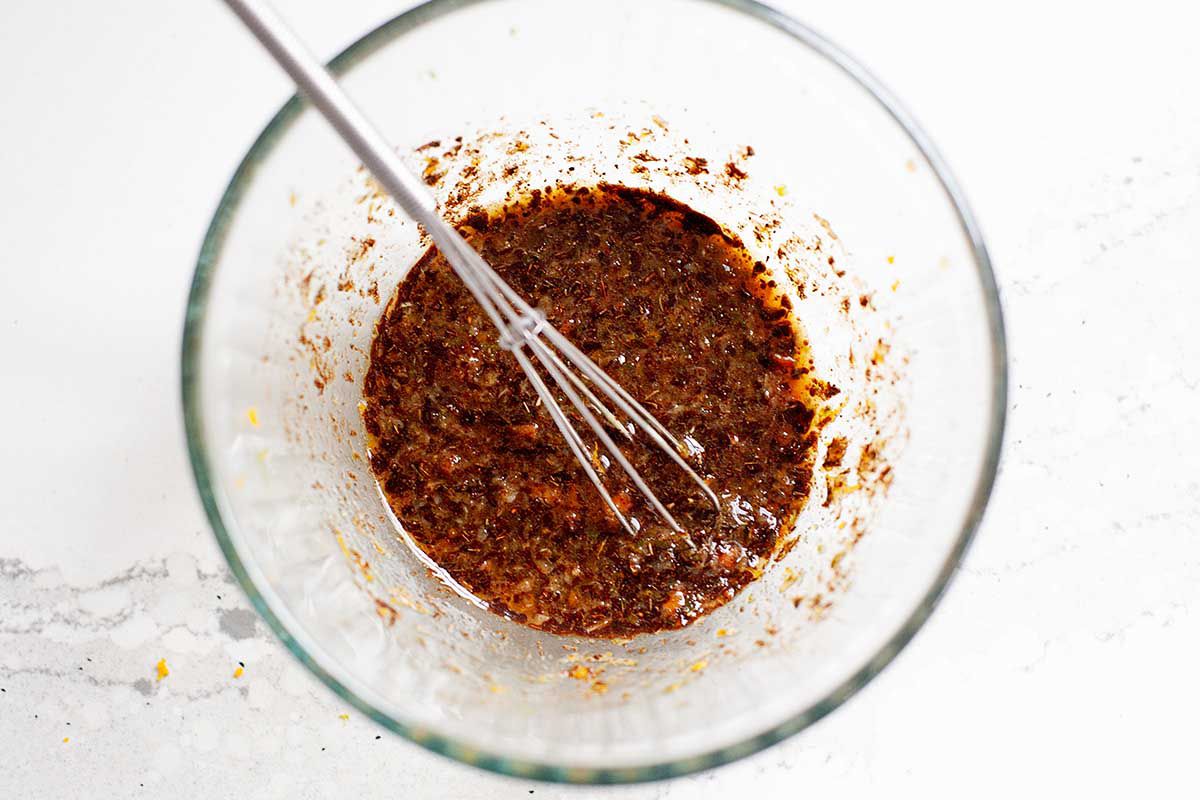 A glass prep bowl with chunky jerk seasoning. A small whisk is in the bowl along with the rub.