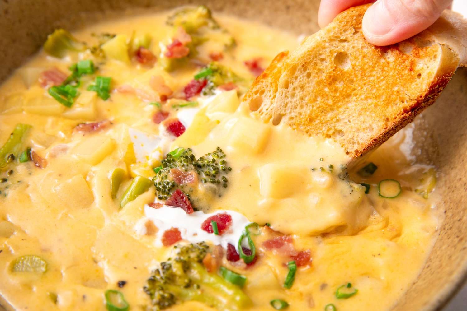 Broccoli potato soup with pieces of bread garnished with green onions and bacon