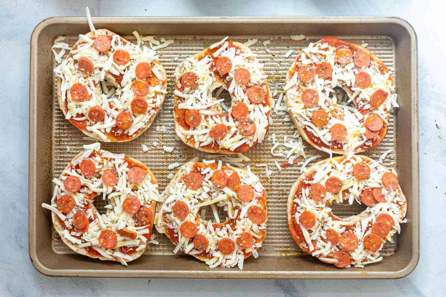 Assembled pizza bagels on a sheet pan. 