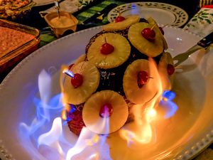 A cooked ham garnished with pineapple slices and cherries surrounded by flames on a serving plate