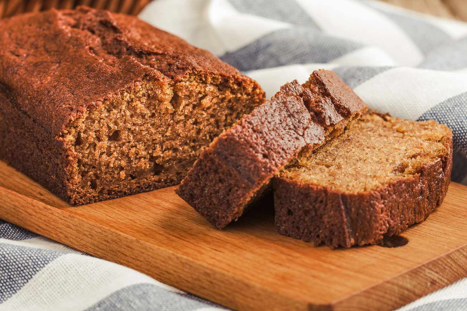 A loaf of spice cake on a wooden board partially sliced with two pieces visible