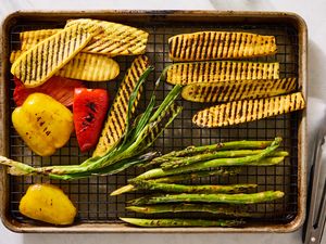 Grilled vegetables including bell peppers, zucchini, and asparagus on a baking sheet with tongs to the side