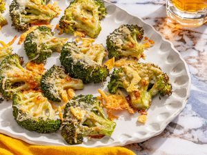 crispy parmesan broccoli on a platter next to a table napkin and a drink in a glass