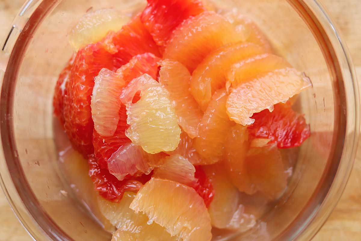 A small bowl of supremed grapefruit and oranges with the juices visible at the bottom of the bowl.