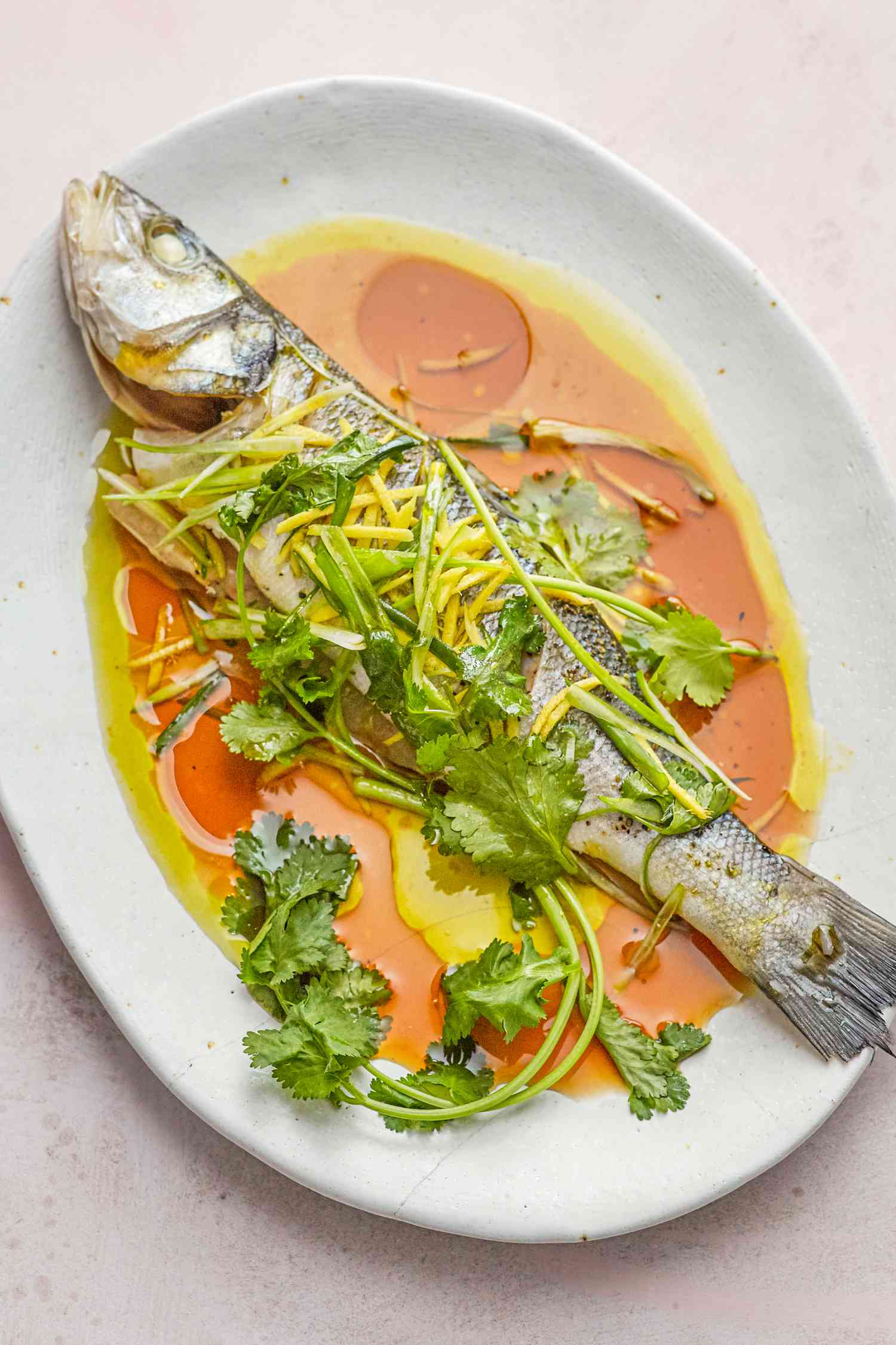 Overhead view of a steamed whole fish on a flatter and topped with sauce and herbs.
