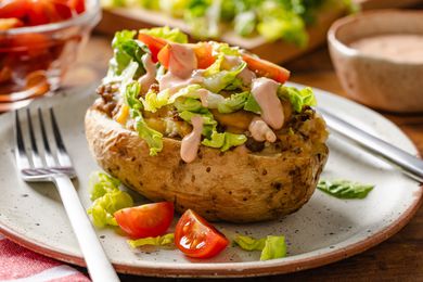 cheeseburger stuffed baked potatoes on a plate at a table setting with bowls of toppings and sauce