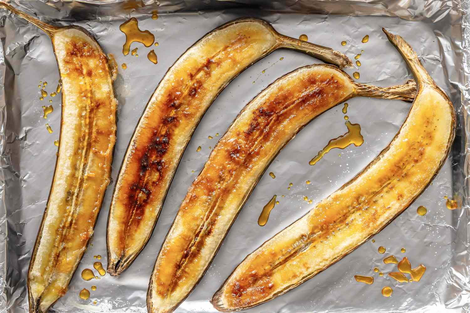 Caramelized banana halves on a foillined tray with syrup drizzles
