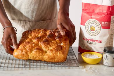 hands placing King Arthur Flour’s Big and Bubbly Focaccia on a cooling rack, flour and salt on the side