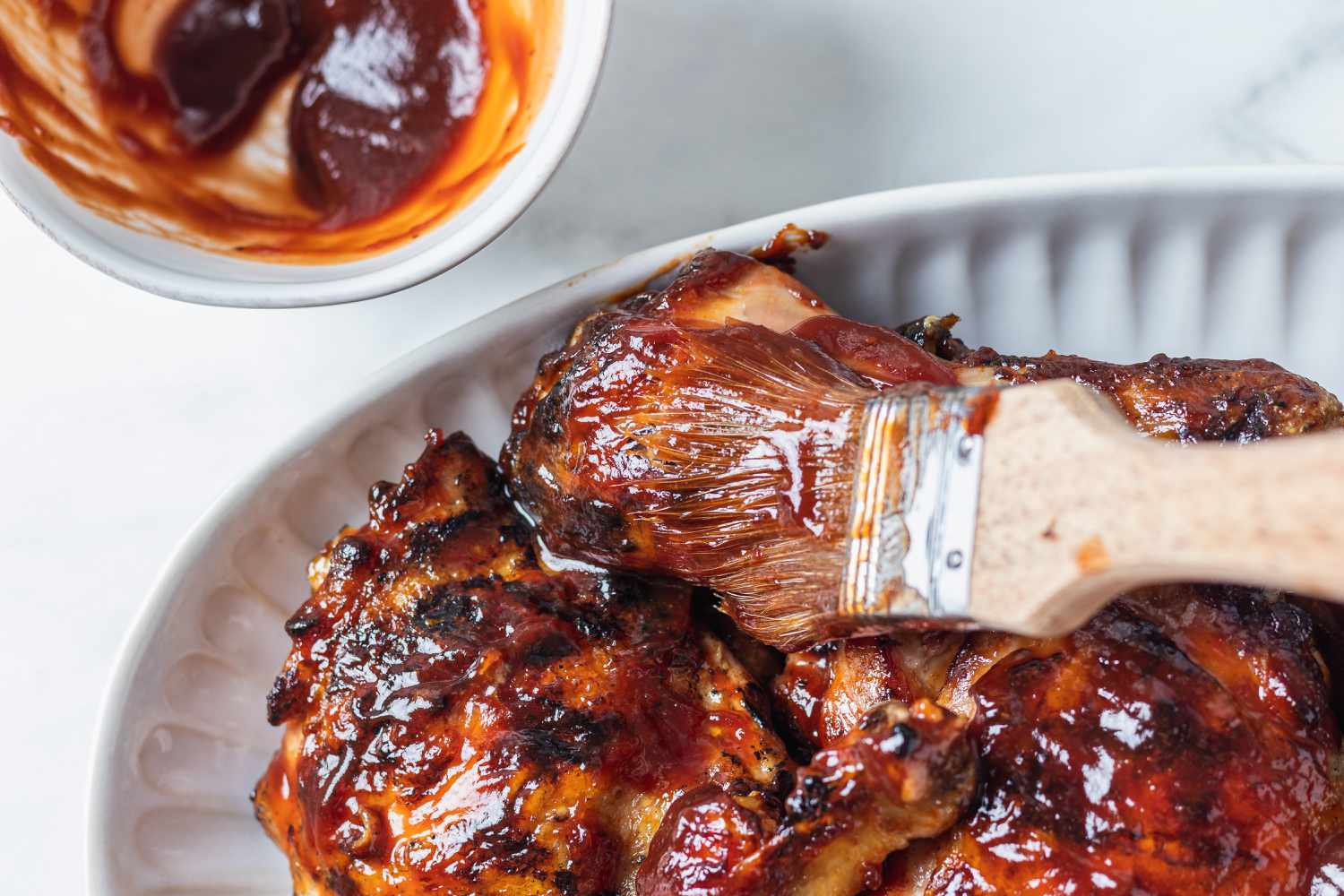 Brushing bbq sauce on grilled bbq chicken on a platter.