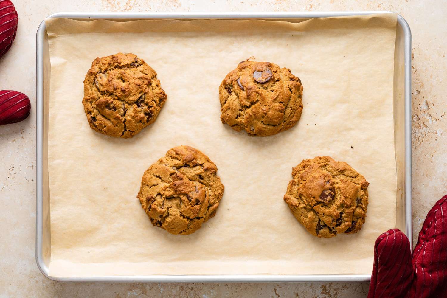 Four chocolate chip cookies on a baking tray lined with parchment paper