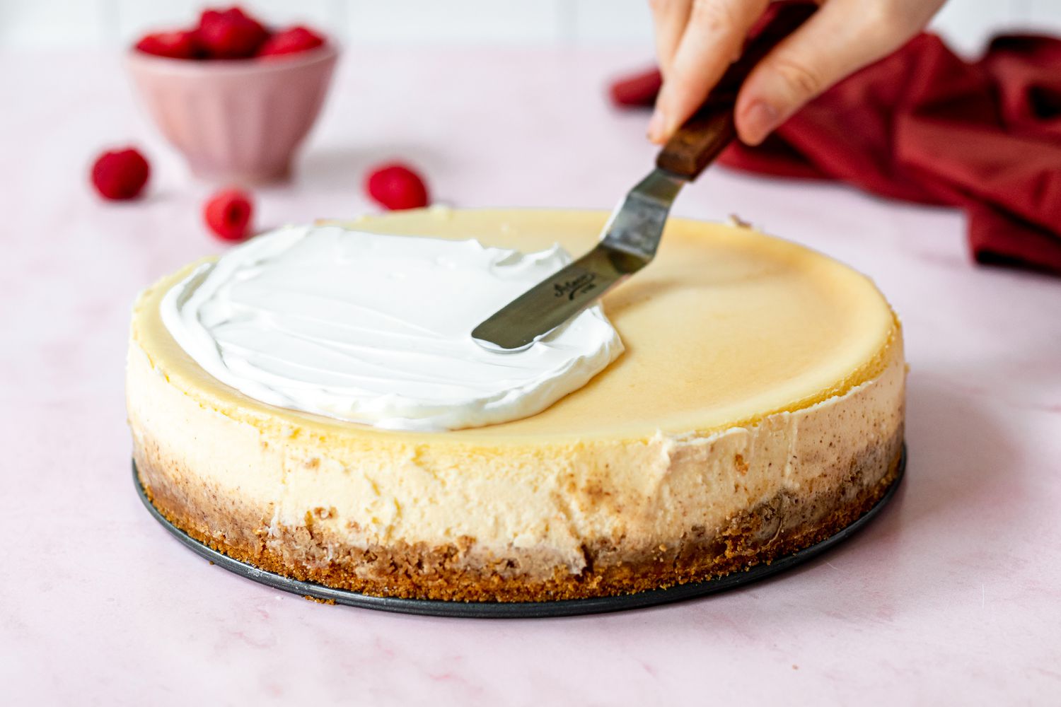 Spreading the cheesecake with a sour cream topping.