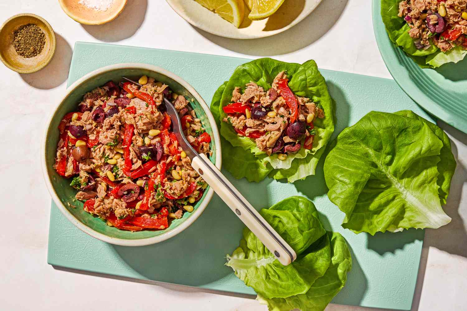Overhead view of a bowl of italian-style tuna salad with a spoon next to one lettuce leaf topped with salad and two plain leaves