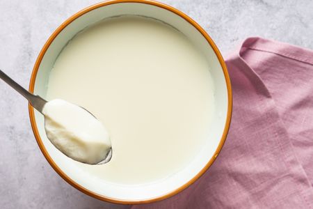 Overhead shot of a bowl of creamy ginger milk pudding with a spoon, pink cloth nearby