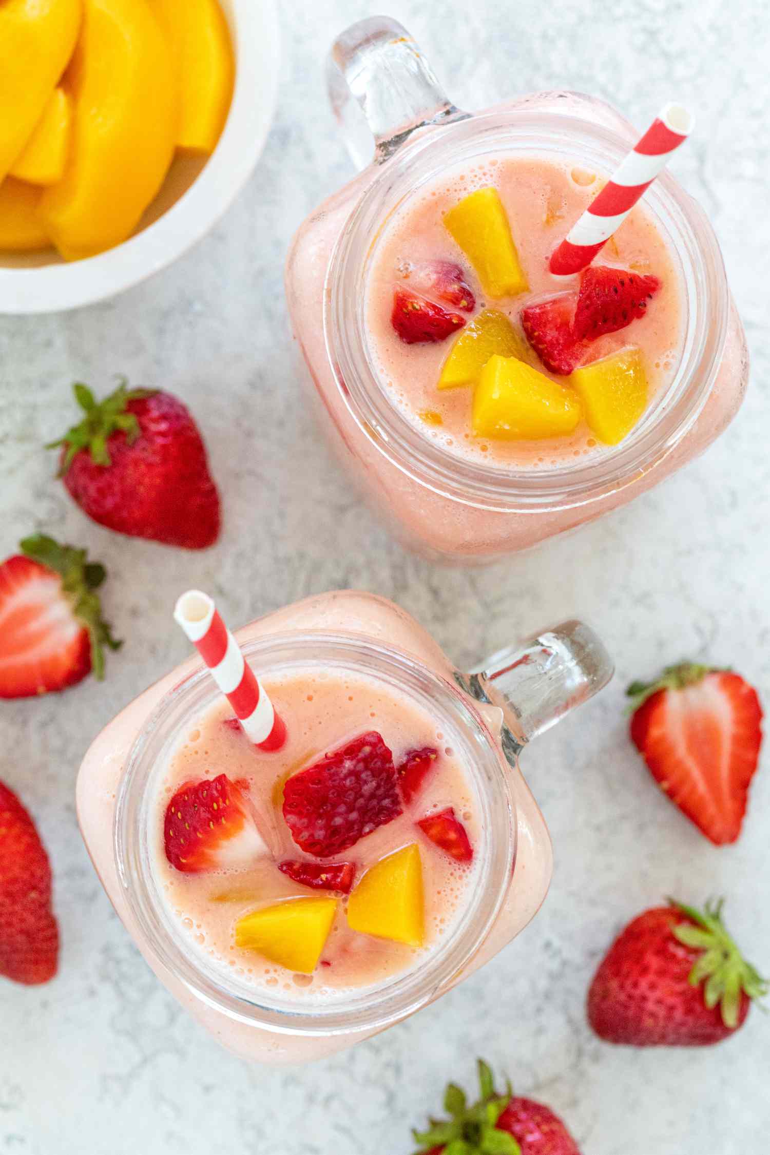 Overhead view of two peach strawberry smoothies topped with fresh fruit.
