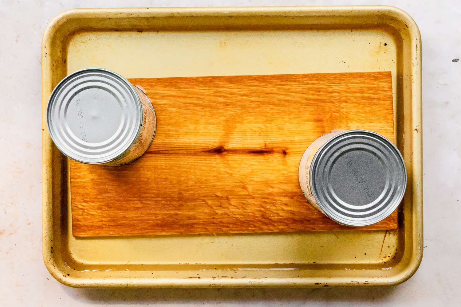 Cedar Plank Soaking in a Water Filled Baking Pan With Two Cans Holdings the Plank Down