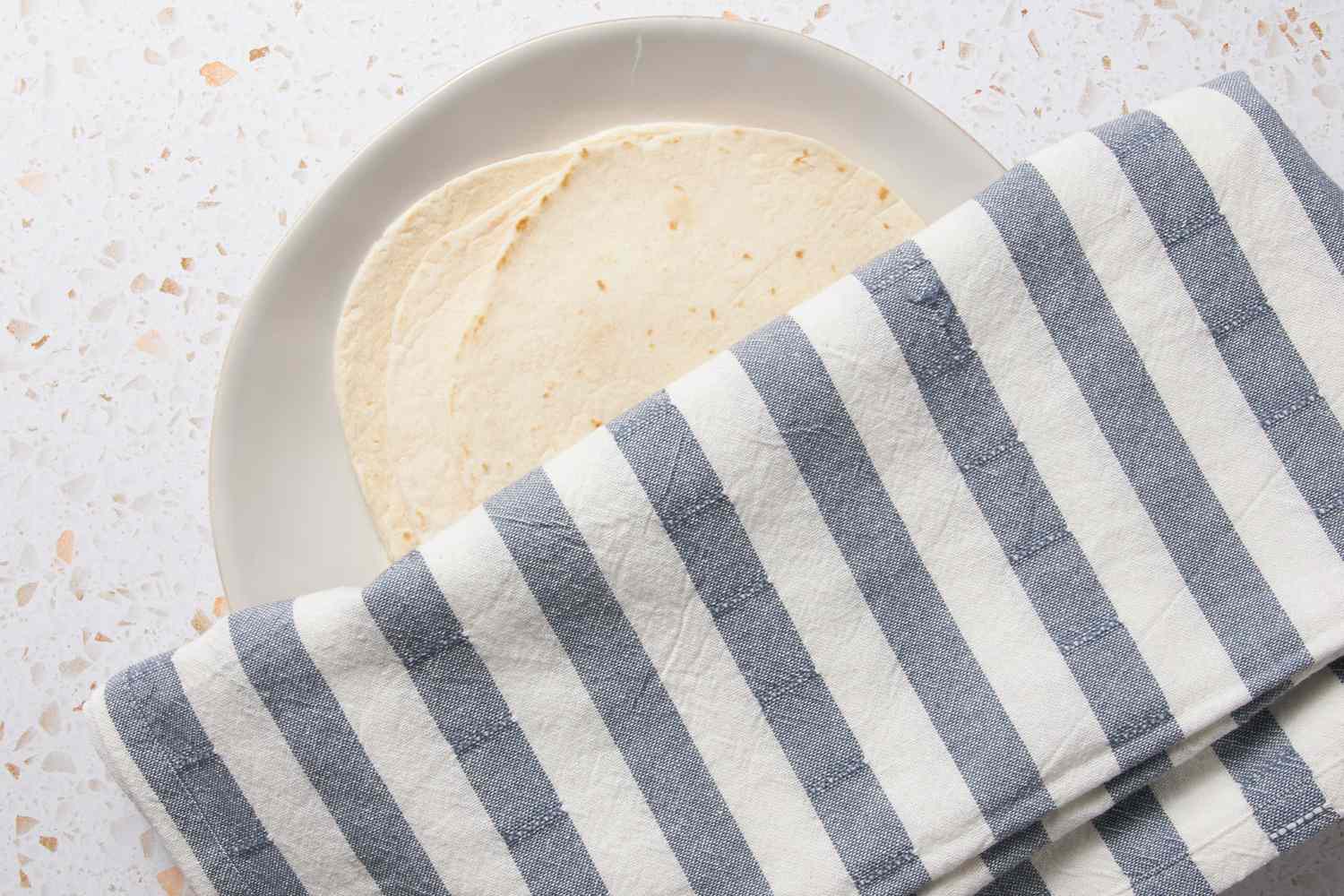 Flour Tortillas on a Plate Partially Covered in a Kitchen Towel