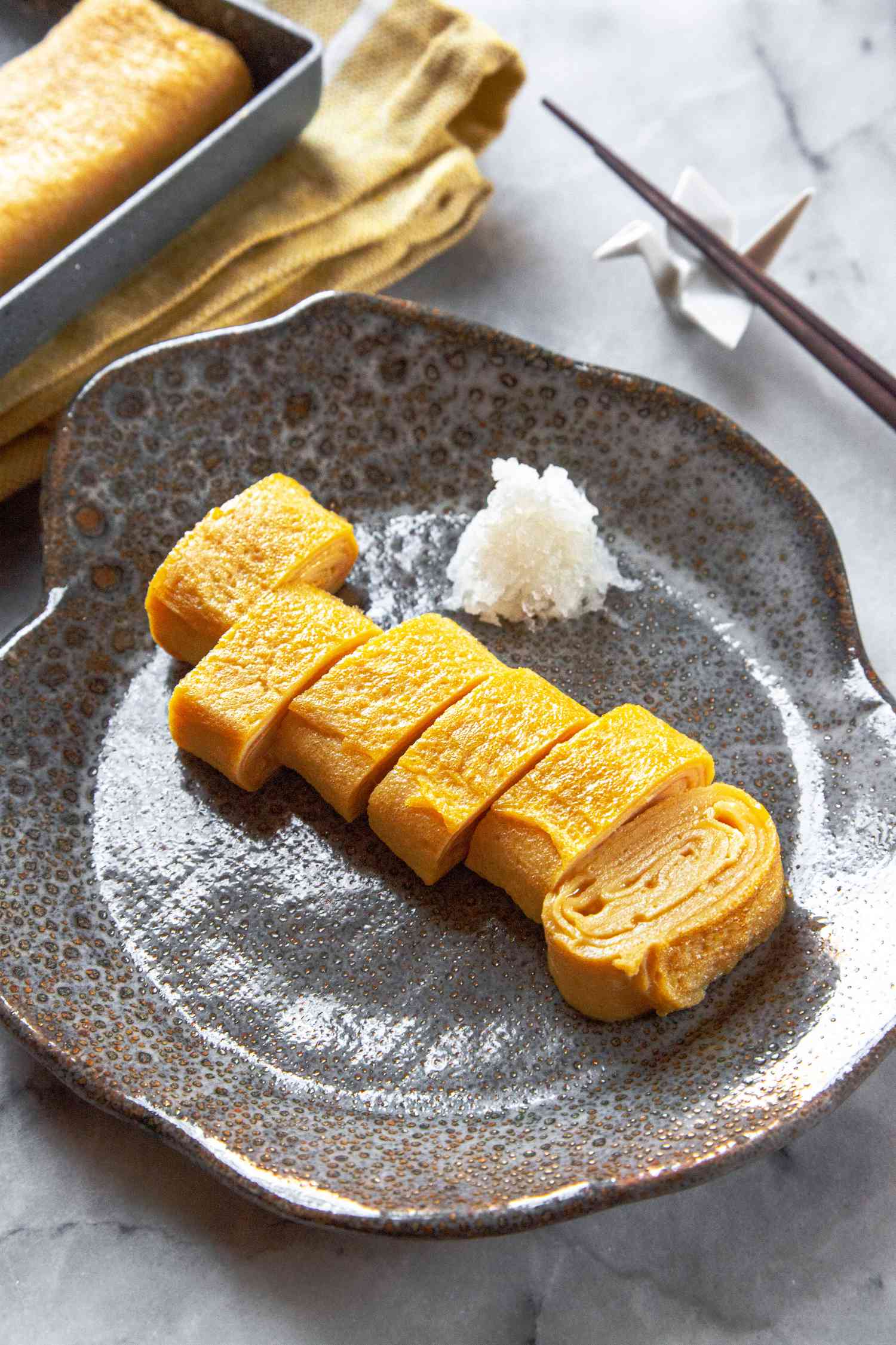 Tamagoyaki Cut into Pieces on Plate with Chopsticks Next to Uncut Tamagoyaki in Pan