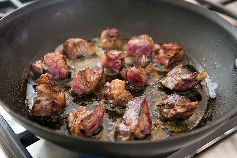 Beef chunks cooked in frying pan to a brown with some red in meat