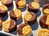 Ritz crackers assembled into ice cream sandwiches, partially dipped in chocolate, on a tray