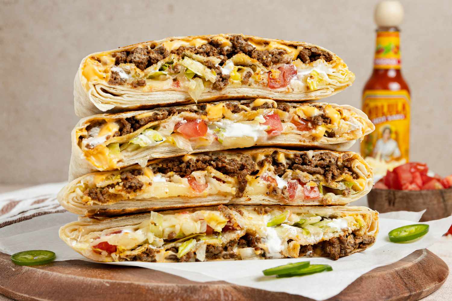 Stack of Copycat Crunchwrap Supreme Cut in Half on Parchment Paper Over a Wooden Board