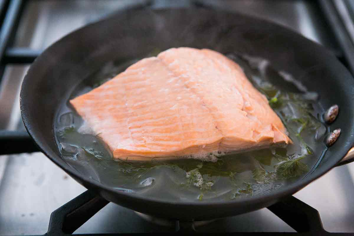Salmon poaching on herbs in a pan