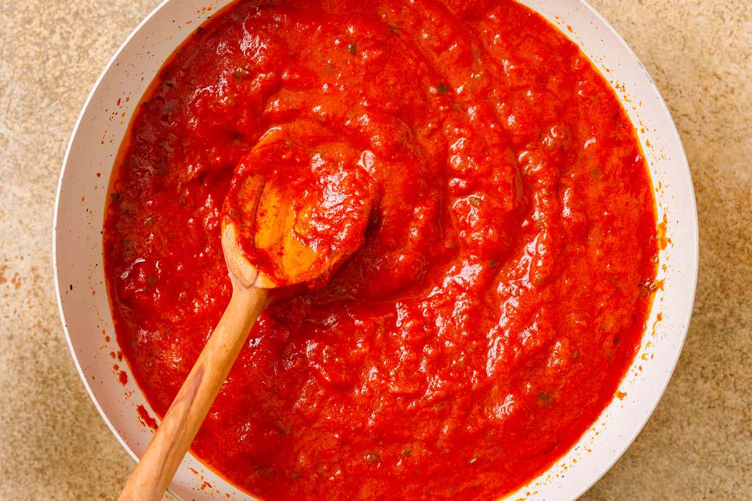 A wooden spoon in a bowl of tomato sauce evenly spread and textured
