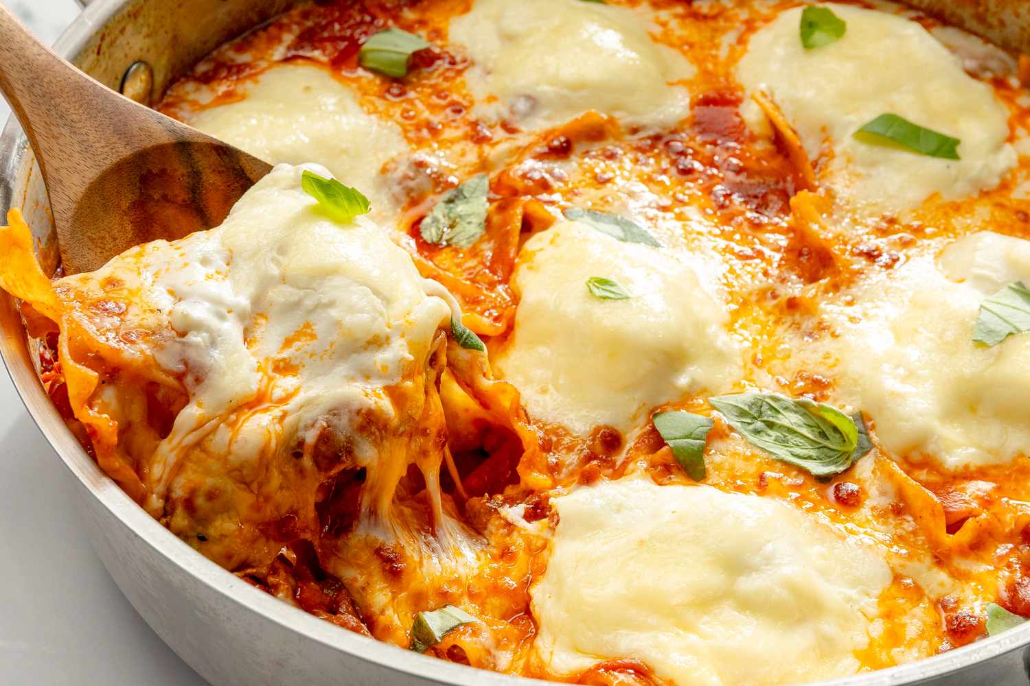 A skillet lasagna being served with a wooden spoon visible layers of pasta sauce and melted cheese