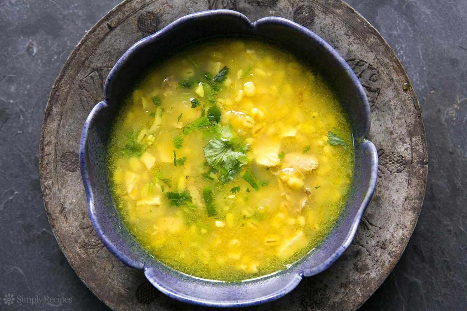 A top shot of a bowl of bright yellow turkey soup with lemon and barley